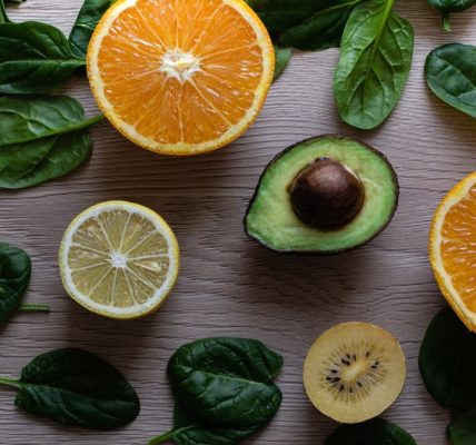 Colorful flat lay of sliced fruits and fresh greens on a wooden table, ideal for healthy lifestyle concepts.