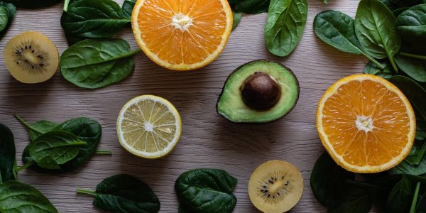 Colorful flat lay of sliced fruits and fresh greens on a wooden table, ideal for healthy lifestyle concepts.